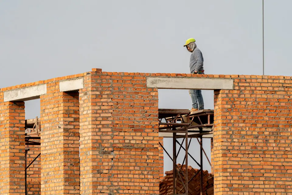 A bricklayer working on top of a rising face brick wall on a building site