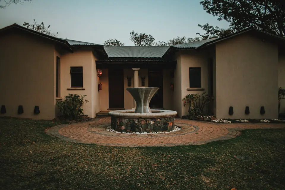 A single storey house at dusk with a lit fountain in the front garden