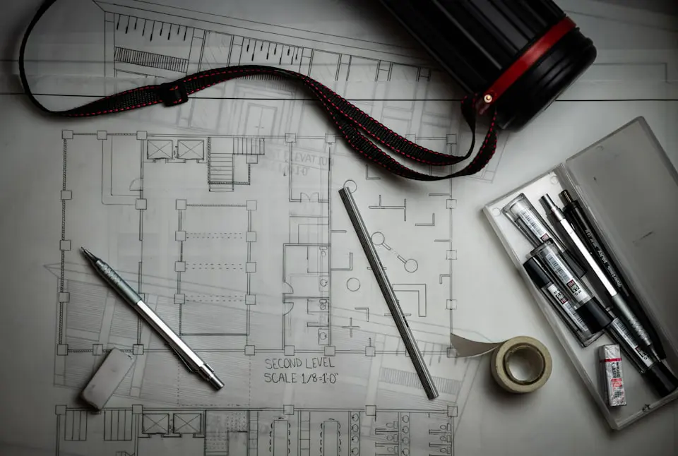 Architectural blueprints laid flat with drafting pencils, a metal scale rule and a drawing tube