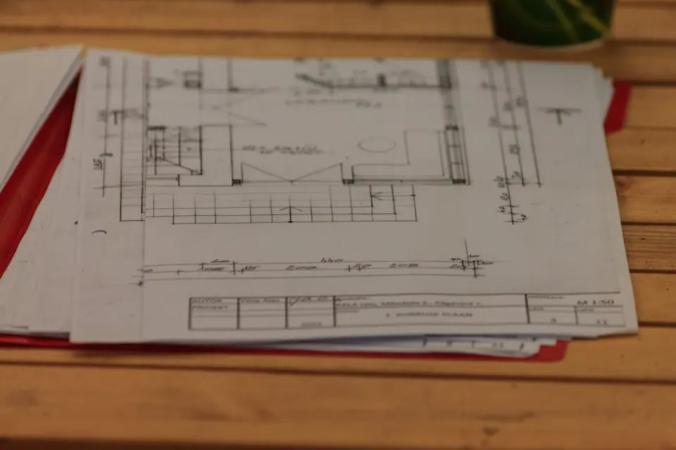 A hand-drawn plan sheet on a wooden table with its title block visible in the corner